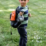 A child holding a leaf blower in a grassy area.