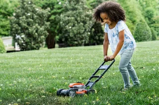 A child mowing the lawn with a push mower in a garden setting.