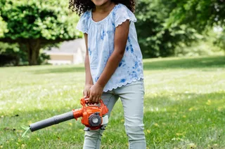 A child holding a leaf blower in a grassy park setting.