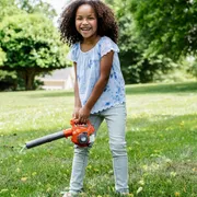 A child holding a leaf blower in a grassy park setting.