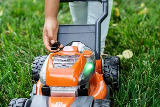 A person adjusting the battery compartment of a lawn mower on grass.