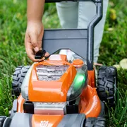 A person adjusting the battery compartment of a lawn mower on grass.