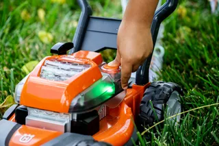 A person adjusting the settings on a Husqvarna lawn mower in a grassy area.
