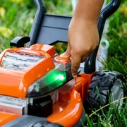 A person adjusting the settings on a Husqvarna lawn mower in a grassy area.