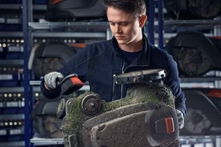 A person inspecting the underside of a Husqvarna robotic lawn mower in a workshop.