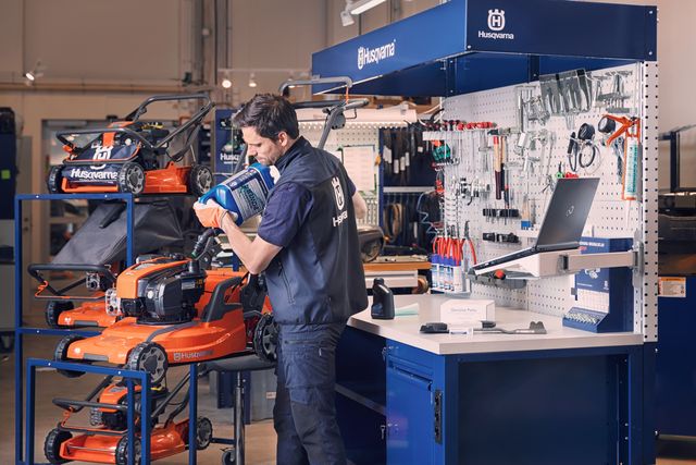 A person working in a workshop with Husqvarna lawn mowers and tools on display.