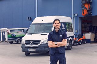 En person står framför en skåpbil och ett lager med Husqvarna-produkter.