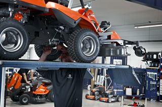 A person working underneath a ride-on mower in a workshop setting.