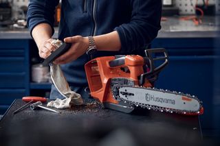 A person cleaning a Husqvarna chainsaw on a workbench.