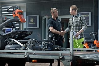 Two people shaking hands next to a Husqvarna ride-on mower on a trailer.