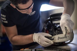 A person adjusting the chain on a Husqvarna chainsaw, with tools on the table.