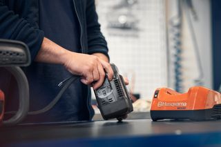 A person handling a Husqvarna battery charger on a workbench.