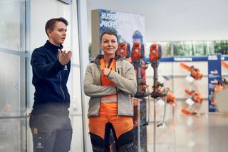 Two people in a showroom discussing Husqvarna professional chainsaws displayed on the wall.