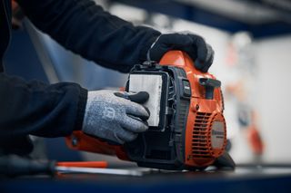 A person replacing the air filter in a Husqvarna chainsaw.