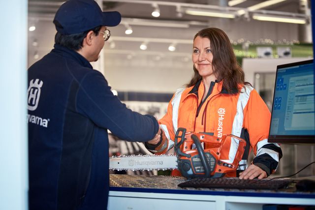 Dos personas dándose la mano sobre una motosierra Husqvarna en el mostrador de una tienda.