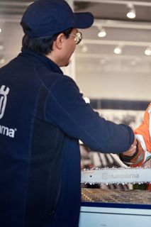 Two people shaking hands over a Husqvarna chainsaw on a counter in a store setting.