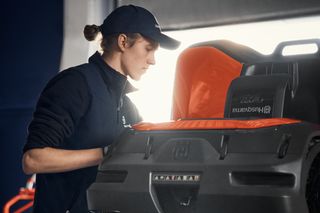 A person inspecting a Husqvarna robotic lawn mower in a workshop setting.