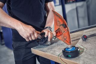 A person assembling a trimmer head on a workbench.