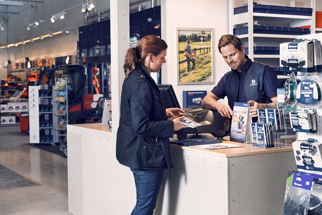 A customer interacting with a store employee at a service counter, with various products displayed around.