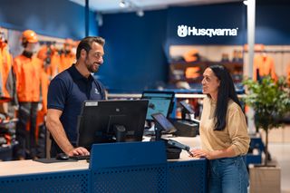 A person interacting with a store employee at a Husqvarna retail counter, with products displayed in the background.