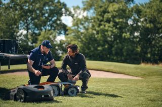 Two people inspecting robotic lawn mowers on a golf course.