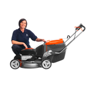 Person kneeling beside a walk-behind lawn mower, accessing engine area, studio side view.