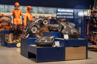 Esposizione di robot tagliaerba in uno showroom con manichini in tenuta da lavoro.