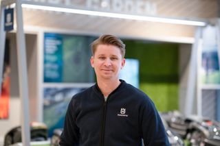 En person som bär en jacka med Husqvarnas varumärke i en butik med olika produkter i bakgrunden.