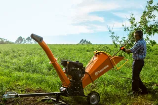 Triturador de Galhos Husqvarna GC 5100PE. Uma pessoa a utilizar um picador de madeira Husqvarna num ambiente exterior relvado.