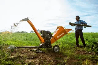 Triturador de Galhos Husqvarna GC 5100PE. Uma pessoa usando um picador de madeira em um ambiente gramado ao ar livre.