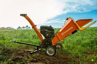 Triturador de Galhos Husqvarna GC 5100PE. Um picador de madeira em um campo, parcialmente visível com rodas e calha.