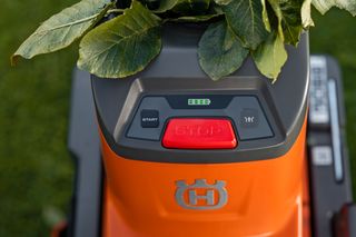 Nahaufnahme eines Rasenmäher-Bedienfelds mit Stopptaste und Batterieanzeige, bedeckt mit Blättern.