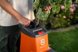 Eine Person, die einen Gartenhäcksler verwendet, um Äste in einem Garten zu verarbeiten.