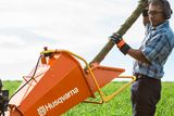 Uma pessoa a alimentar um ramo num picador de madeira Husqvarna numa área com relvado.