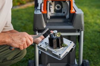 Eine Person, die ein Gartenhäckselmesser mit einer Bürste reinigt.