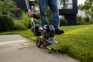 Une personne utilise un coupe-bordures pour délimiter une pelouse le long d’un chemin pavé.