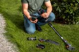 Людина, яка збирає садові кущоріз Husqvarna на газоні з розкладеними різними насадками.