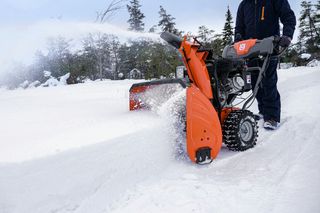 A person operating a snow blower to clear snow in a snowy landscape.