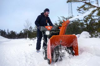 A person operating a snow blower in a snowy landscape.