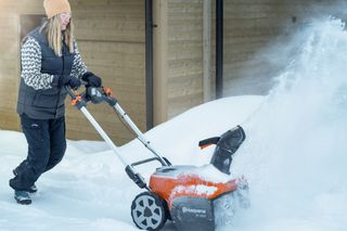 En person som bruker en snøfreser for å rydde snø i et boligområde.
