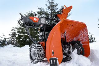 A snow blower clearing snow in a snowy landscape with trees in the background.