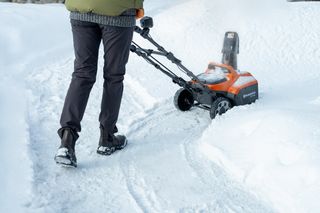 En person som bruker en snøfreser til å rydde snø fra en gangvei.