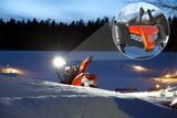 Eine Schneefräse, die in der Abenddämmerung in einer verschneiten Landschaft arbeitet, mit einer Nahaufnahme des Bedienfelds.