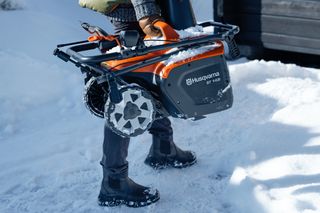 Husqvarna hófúvót hordozó személy havas kültéri környezetben.