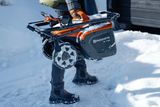 Osoba niosąca odśnieżarkę Husqvarna w zaśnieżonym otoczeniu na zewnątrz.