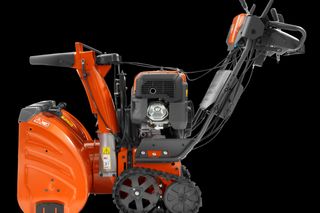 Side view of a snow blower with visible engine and control panel.