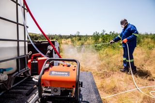 Людина в робочому спорядженні використовує обприскувач Husqvarna в полі.