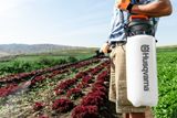 A person using a Husqvarna garden sprayer in a field with crops.