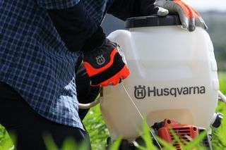 Людина, яка використовує ранцевий обприскувач Husqvarna в полі.