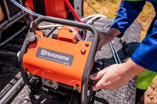 Людина, яка налаштовує електроінструмент Husqvarna на верстаку надворі.